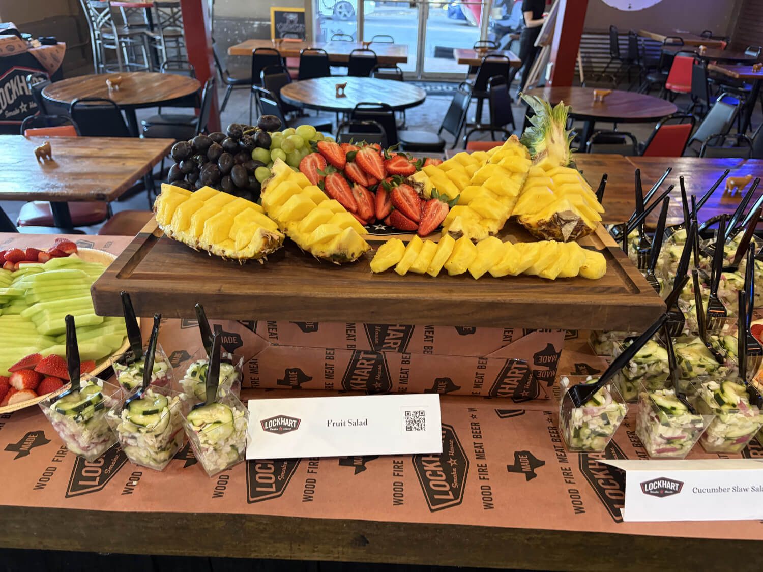Fruit display on a wooden board with pineapple wedges, strawberries, grapes, and melon slices in a cafe setting